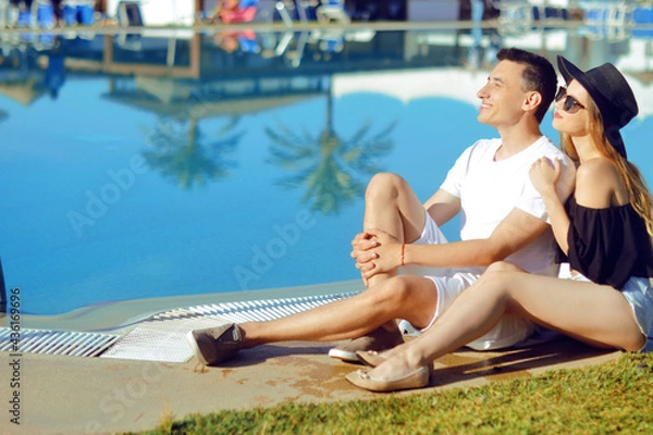 Fototapeta  A sunny day, a man and a girl enjoy the rest. Travel. Against the background of palm trees and houses. Couple at the hotel with a pool. The concept of relaxation and travel. Kiss