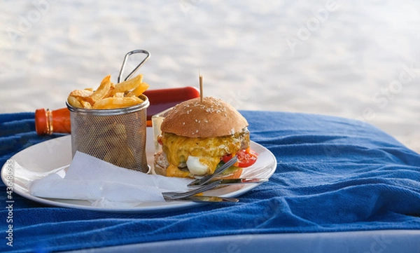 Obraz Classic beef burger with cheese and french fries. on white plate. Fast food on the beach. Blue background. Selective focus.