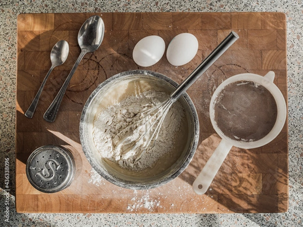 Fototapeta Top view of a wooden board with ingredients for making pancake dough. Composition with kitchen utensils, eggs, salt and flour. Cooking concept.