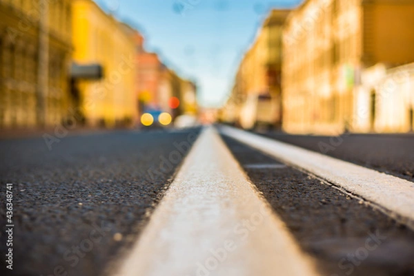 Fototapeta Clear day in the big city, empty city street and headlights moving car. View of the road at the level of the dividing line