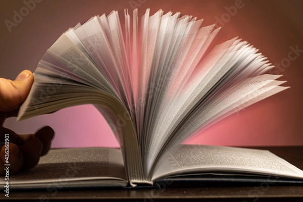 Fototapeta flipping through the pages of an open book on a red background