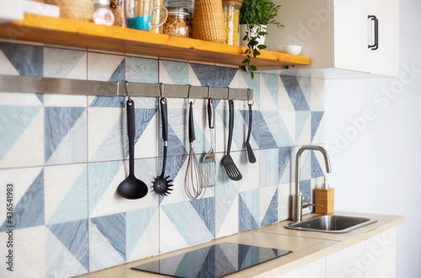 Fototapeta Kitchen spatulas handing on railing on a tiled wall with blue geometric pattern