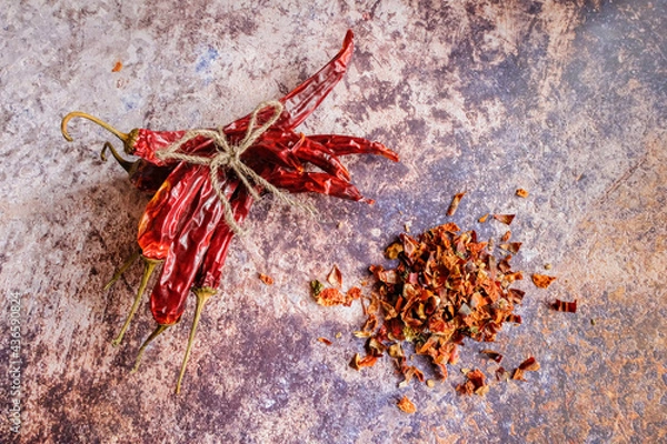 Fototapeta Pile of crushed red pepper, Cayenne pepper, dried chilli on a motley background. Next to a bunch of whole dry chili peppers. It is a popular spicy condiment for Mexican dishes.