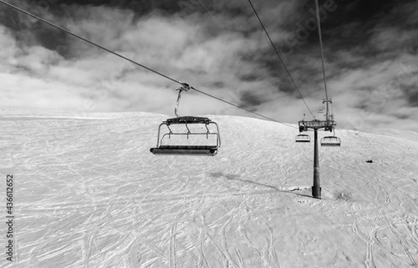 Fototapeta Black and white snowy off-piste ski slope, chair-lift on ski resort and sky with clouds