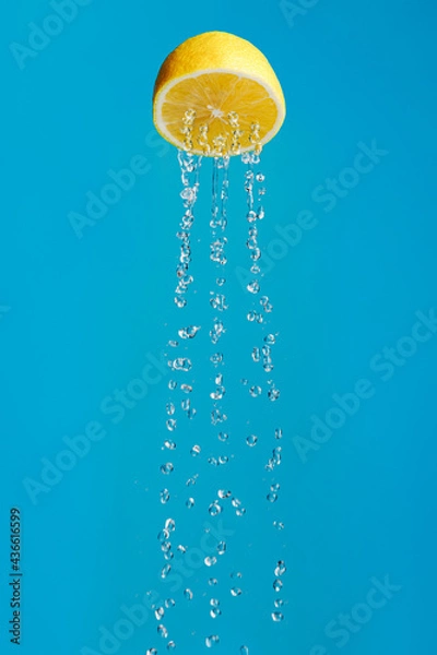 Obraz Lemon as a metaphor for a shower isolated on a blue background. Creative fruit food or drink concept. Lemon juice as a favorite summer refreshing drink with rain, splash and drops.