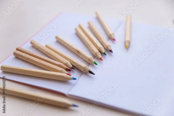 Fototapeta Open white notebook, with colored crayons beside it, penknife and drawing of a colored flower. 