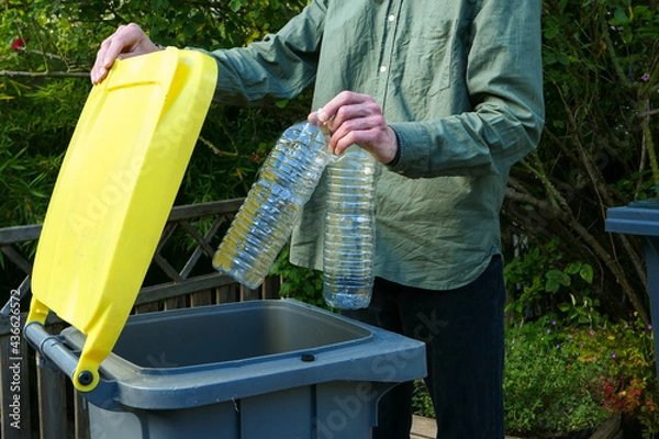 Fototapeta One person making a selective sorting of waste. Man putting plastic bottles in a yellow bin for recycling.	
