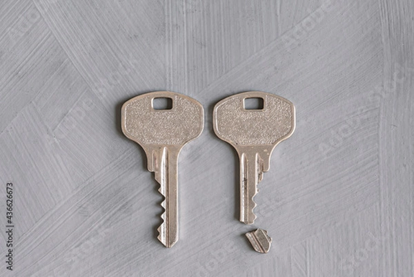 Fototapeta Two broken and whole keys on a gray textured background. Conceptual symbolic image