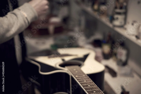 Fototapeta A service worker repairs a guitar with a tool.