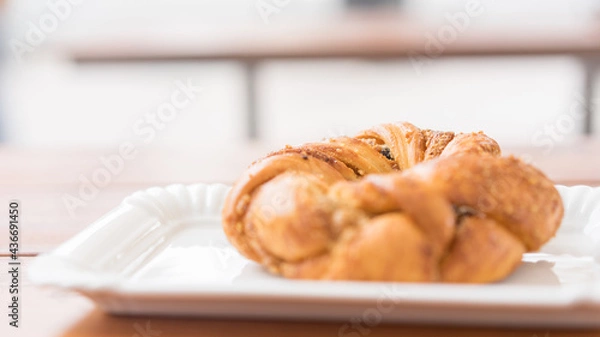 Fototapeta Freshly baked bagel on a white flat plate in a bakery on a table outdoors. Selective focus. Beautiful bokeh
