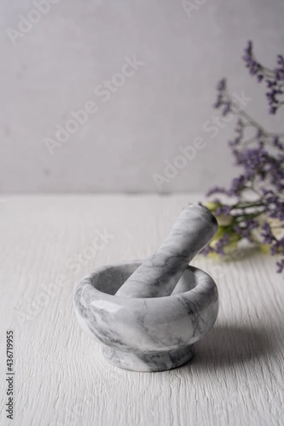 Obraz On a white textured background is a granite mortar for grinding spices. The kitchen mortar is made of white marble. In the background, Provencal herbs. Natural materials. Cooking at home.