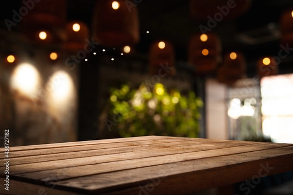 Fototapeta empty wooden table on blurred light gold bokeh of cafe-restaurant window on dark background, place for your products, blurred cafe interior.