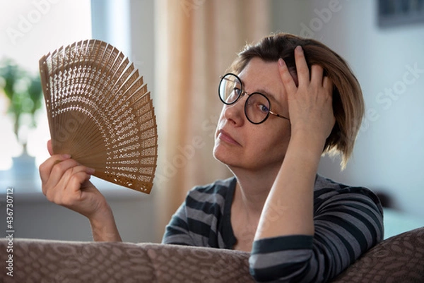 Fototapeta Exhausted middle aged woman waving her fan, suffering from menopausal symptoms, experiencing hot flush. 