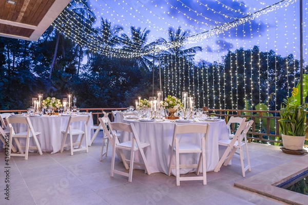 Fototapeta Table Spread no people tropical location with gold cutlery white table cloth and scenic view Romantic Wedding Table Top Layout copy space tablescape soft lighting blue hour