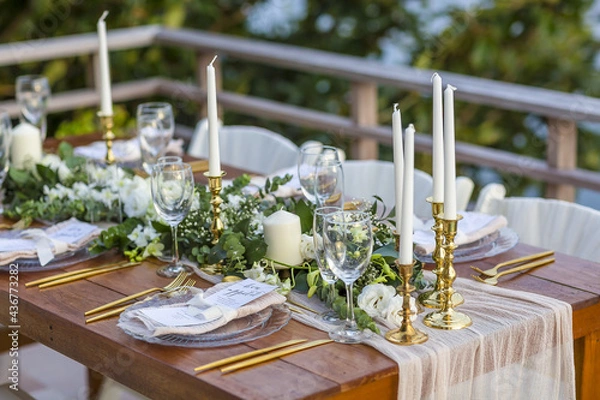 Fototapeta Romantic Wedding Table Top Layout Table Spread with flowers no people with gold cutlery white table cloth and scenic view of sunset and blue skies with copy space tablescape