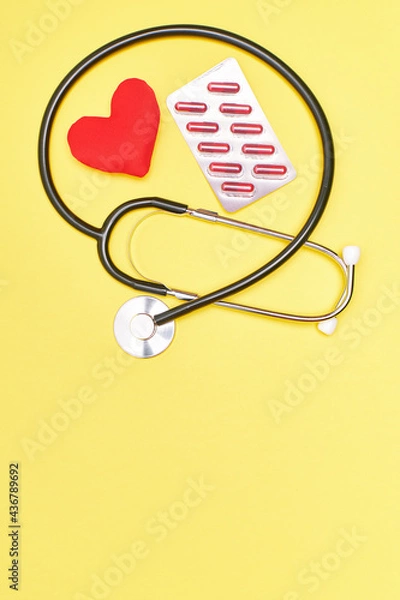 Fototapeta Vertical. Stethoscope with a red heart and pills on a yellow background