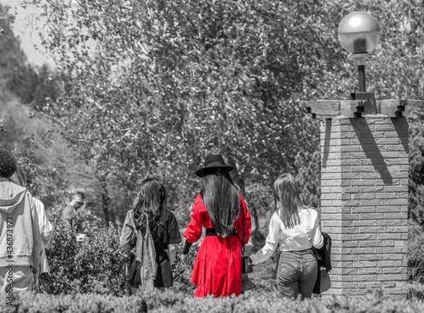 Fototapeta Girl with a red coat and a black hat walking in the park. Selective color.
