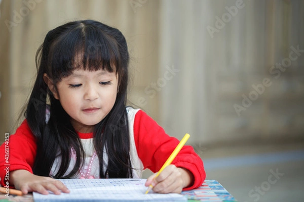 Fototapeta Asian little girl learning and writing in notebook with pencil
