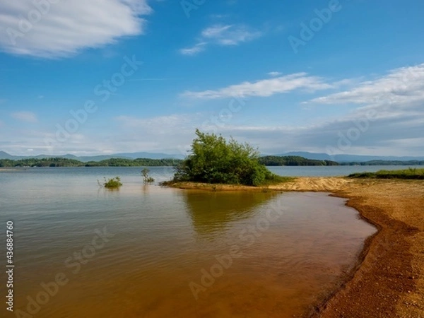 Fototapeta Douglas Lake in the spring in Tennessee with the Great Smoky Mountains in the background, the water and sandy shore with a blue sky filled with clouds in the distance.