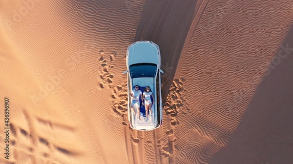 Fototapeta AERIAL. Top view of young couple relaxing on the car's roof at the desert.