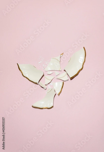 Obraz Broken wedding plate in flying bird shape in ivory color with gold edges against powdery pink background. Minimal artistic flat lay party concept.