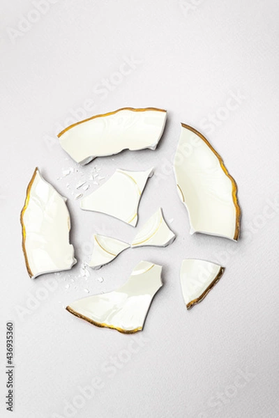 Obraz Broken wedding plate in circle shape in ivory color with gold edges against light gray background. Minimal creative party concept.