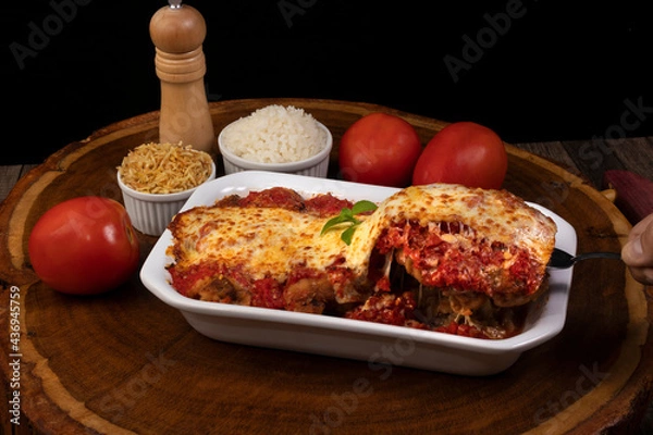 Obraz Steak Parmegiana or Parmegian Filet, made with breaded steak, tomato sauce, cheese au gratin. Accompanied by white rice and potato straw. Hand picking up food with spatula to serve.