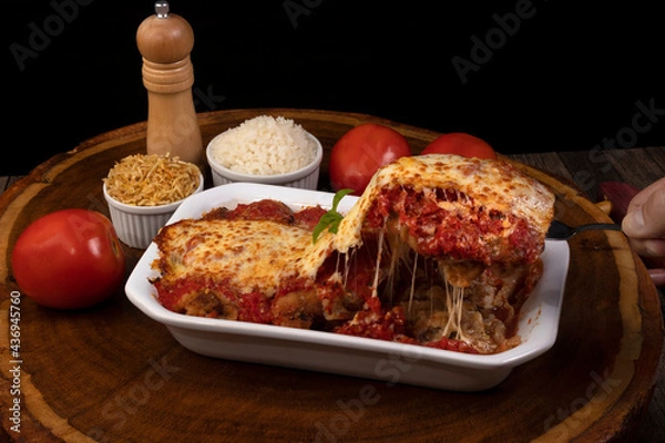 Fototapeta Steak Parmegiana or Parmegian Filet, made with breaded steak, tomato sauce, cheese au gratin. Accompanied by white rice and potato straw. Hand picking up piece with spatula to serve.