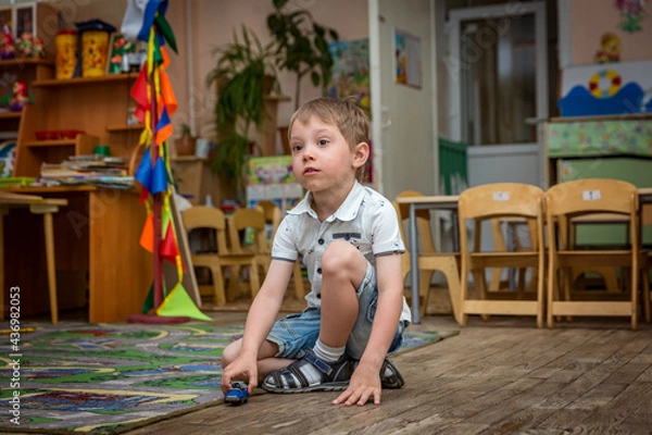 Obraz cute sad caucasian boy sitting alone on the floor in kindergarden playing with a toy car. Image with selective focus