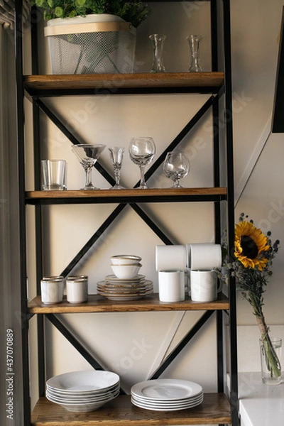Obraz A rack of white dishes stands against a white wall. Next to it is a bouquet of wildflowers: sunflowers and blue thorns. The kitchen is in the style of Provence. Summer mood. Shelf in the kitchen. 