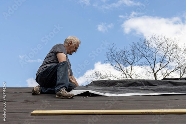 Obraz roofer putting down tar paper on roof
