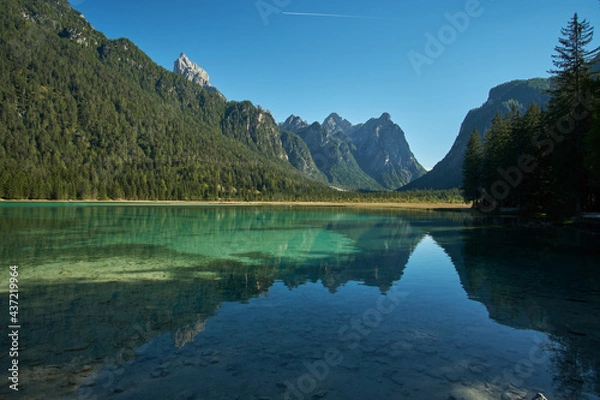 Fototapeta Beautiful mirror reflections in the crystal clear water of Toblacher See lake surrounded by forest and mountains with the Dolomites in the background in Tyrol, Northern Italy. 