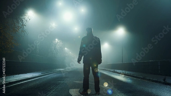 Fototapeta A UFO concept of glowing orbs, floating above a misty winters road at night. With a silhouetted figure , back to camera, looking at the lights.