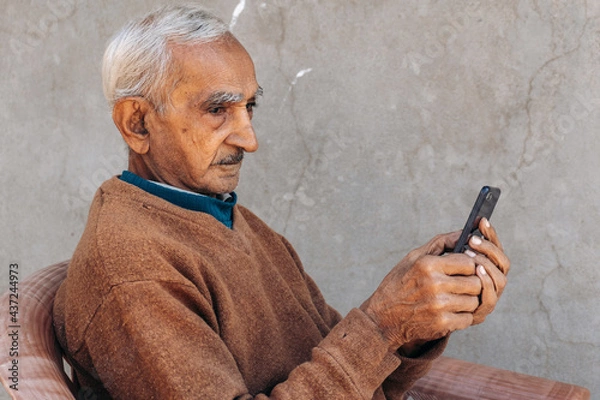 Obraz Side view of Senior old Indian man using mobile phone and typing sms, doing online shopping. Modern lifestyle of old people with technology. Copy space in grey background