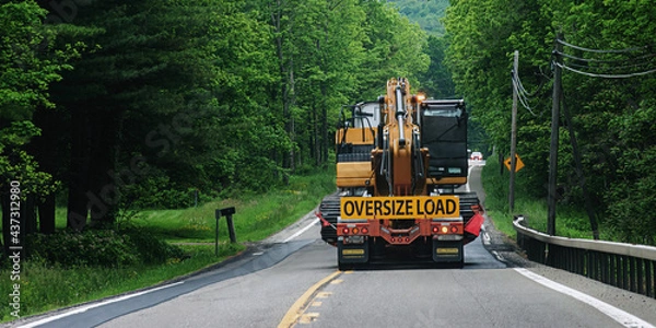Obraz A truck carrying an oversize load is heading toward an oncoming car on Route 79 in the small town of Windsor in Broome County in Upstate NY. Taking up 2 lanes of rural road.