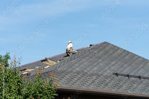 Obraz The man on the roof. Photo of a worker repairing the roof of the house.
