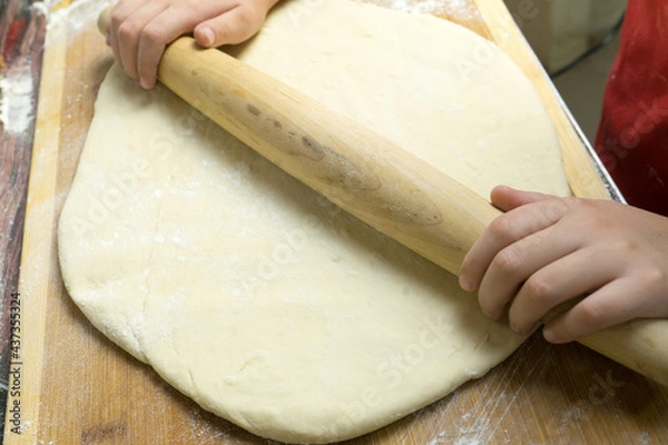 Fototapeta Photo of the hands of a man who rolls the dough with a rolling pin.