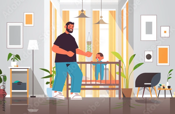 Fototapeta young father playing with little son in crib fatherhood parenting concept dad spending time with his kid at home
