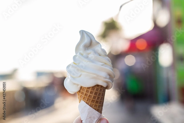 Fototapeta hand held soft serve vanilla ice cream cone outside on a hot summer day in a beach outdoor area boardwalk  stock photo 