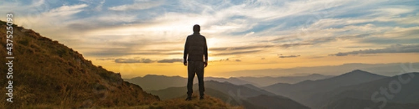 Fototapeta The man standing on the rock with a picturesque sunset