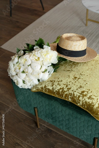 Obraz A straw hat sits next to a bouquet of white peonies on a green pouf.  Romantic summer mood. Stylish interior. White flowers in a bouquet. Give flowers. Outdoor recreation.