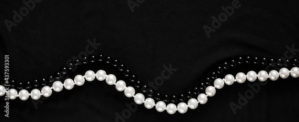 Fototapeta Banner in a dark key with two strings of pearl beads in white and black colors on a gray fabric. An elegant banner with space for text about luxury and the pearl industry.