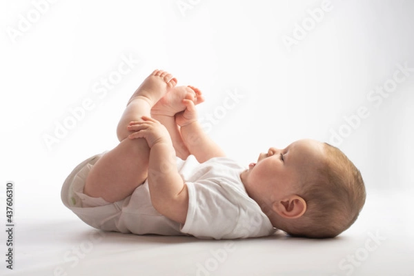 Fototapeta baby lies on his back, holding his legs, on a white background