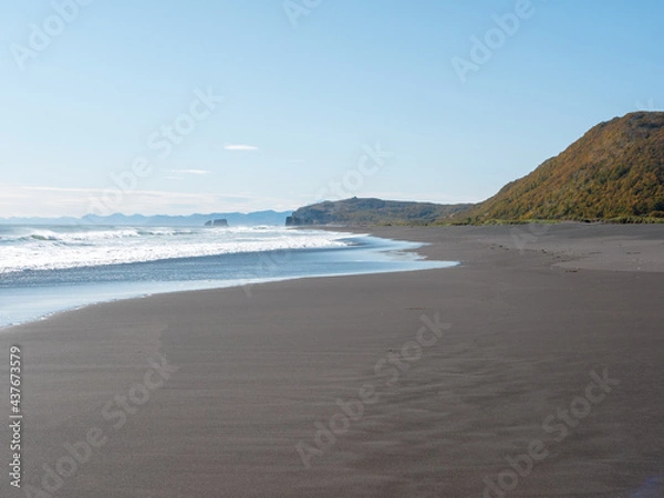 Fototapeta View from the Khalaktyrsky beach to the Pacific Ocean against the background of the blue sky. On the horizon of the black sand beach, cliffs and ocean waves are visible. Kamchatka Peninsula, Russia.