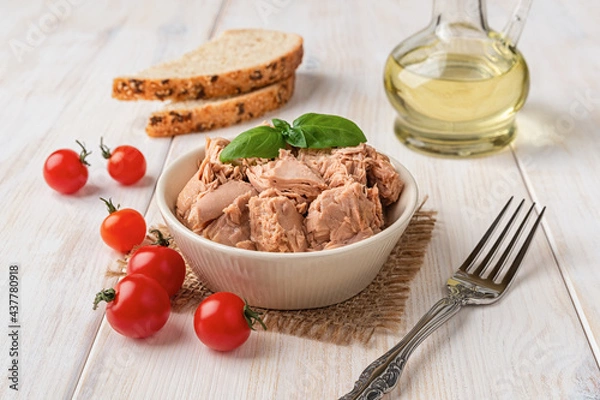 Obraz Canned tuna meat in a bowl, fork, bread and fresh red cherry tomatoes on a white wooden table. Low calories healthy eating snack of preserved tuna fish and vegetables. Tasty seafood.