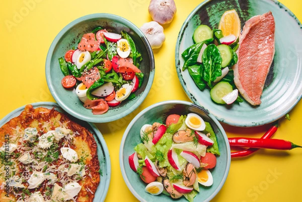 Fototapeta Salad with spinach, eggs and radish in a bowl over bright yellow background. Fish fillet steak, potato and cheese pizza.