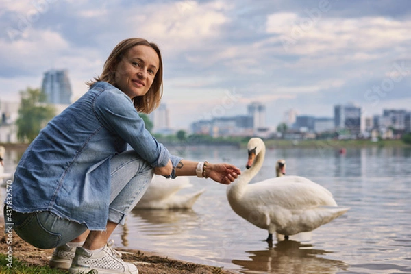 Obraz A caucasian woman laughs and feeds swans by the water. High quality photo