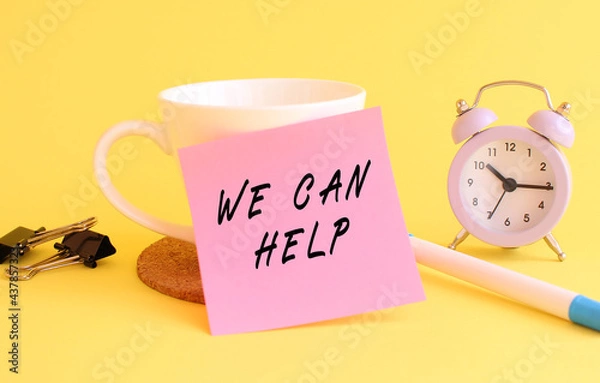 Fototapeta Pink paper with the text WE CAN HELP on a white cup. Clock, pen on a yellow background.