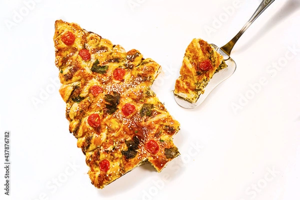 Fototapeta Homemade Christmas cake in the shape of a Christmas tree on a white background. Fresh pastries with tomatoes and cheese decorated with greenery.
