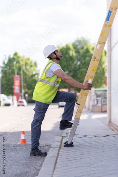 Fototapeta telecommunication technician working at height with ladder and safety helmet
